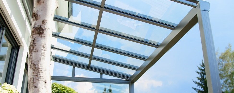 Transparentes Terrassendach mit Wetterschutzelement vor Himmel