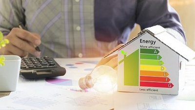 Haus mit Energieeffizienz-Bewertung neben Glühbirne, Mann mit Taschenrechner im Hintergrund
