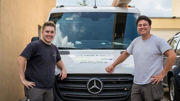 Zwei HEIM & HAUS Handwerker, die an ihrem Fahrzeug lehnen