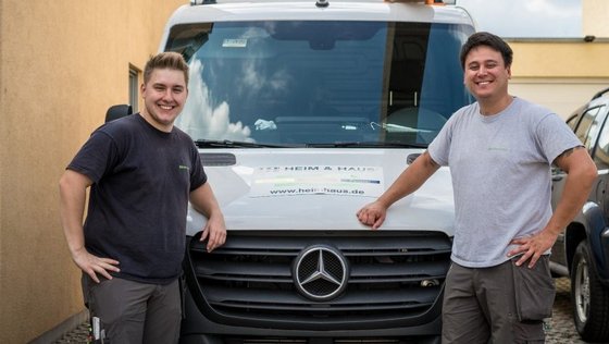 Zwei HEIM & HAUS Handwerker, die an ihrem Fahrzeug lehnen
