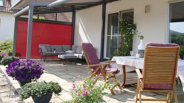 Farbenfrohe Akzente sorgen für ein optisches Highlight Terrasse Sitzgruppe und rotem Zipscreen im Hintergrund