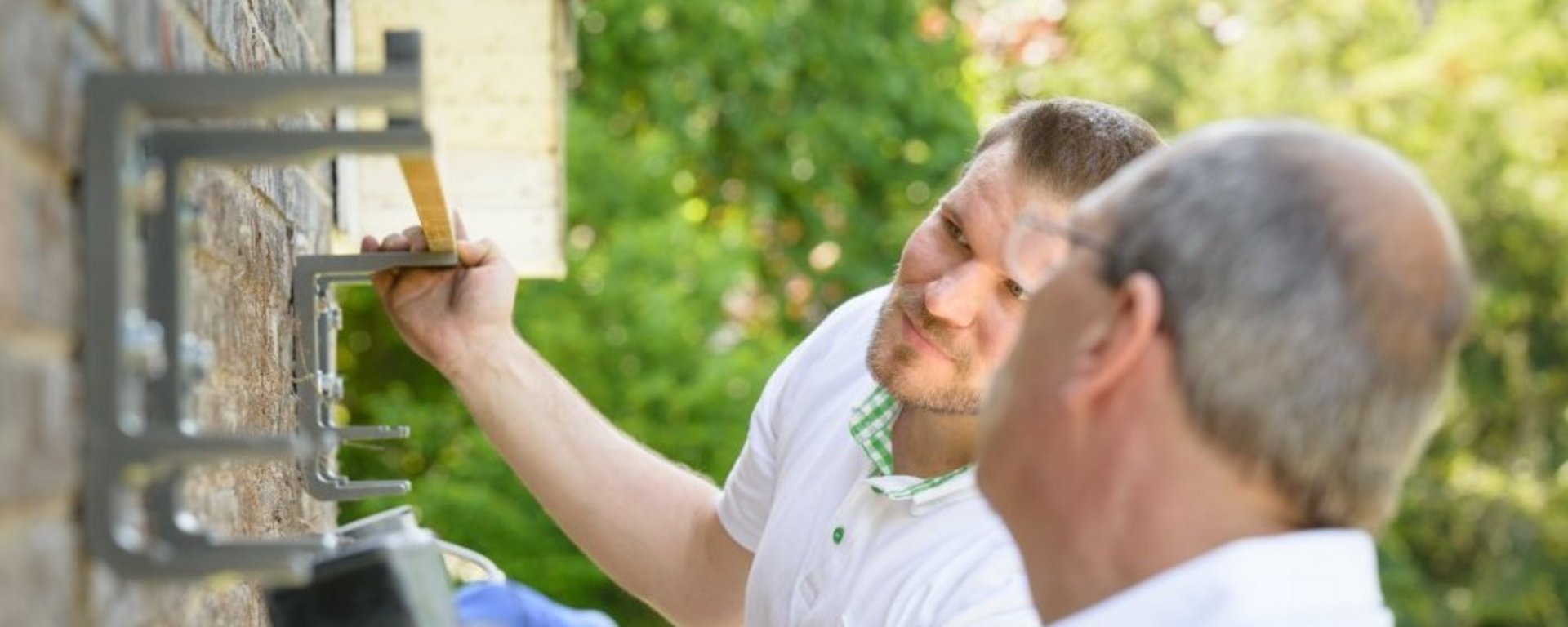 HEIM & HAUS Montagepartner Zwei Montagepartner die etwas an der Außenhauswand befestigen und ausmessen