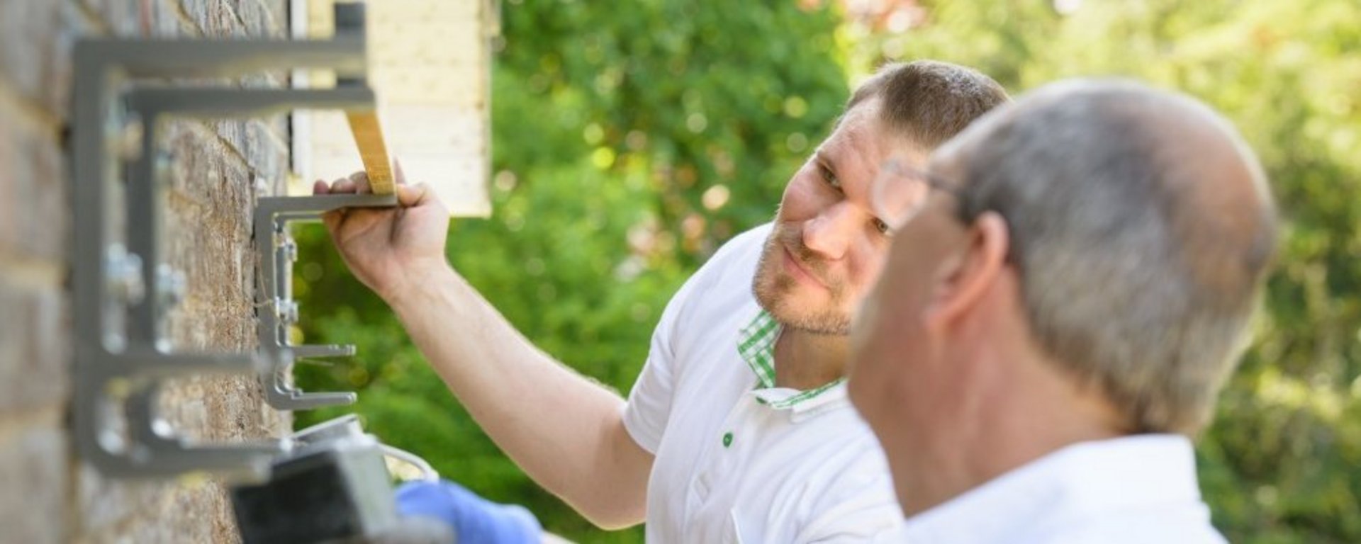 Zwei Montagepartner die etwas an der Außenhauswand befestigen und ausmessen