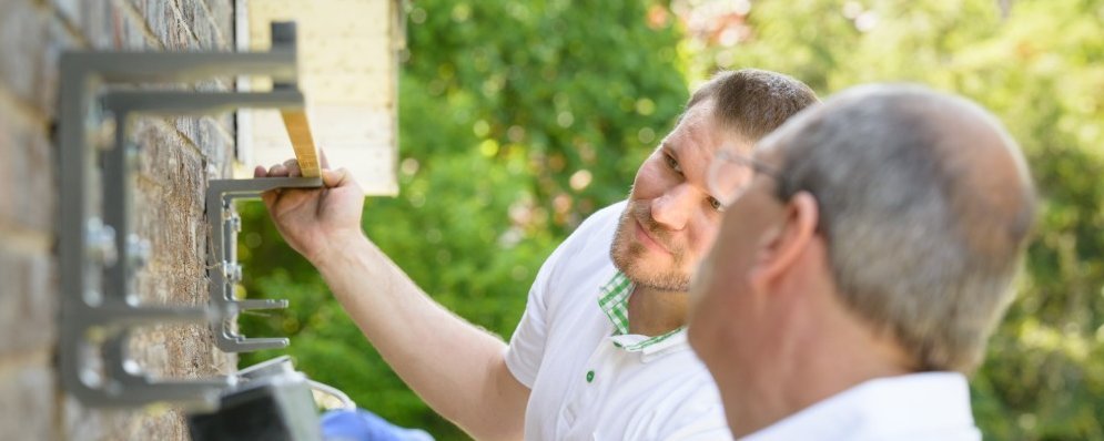 Zwei Montagepartner die etwas an der Außenhauswand befestigen und ausmessen