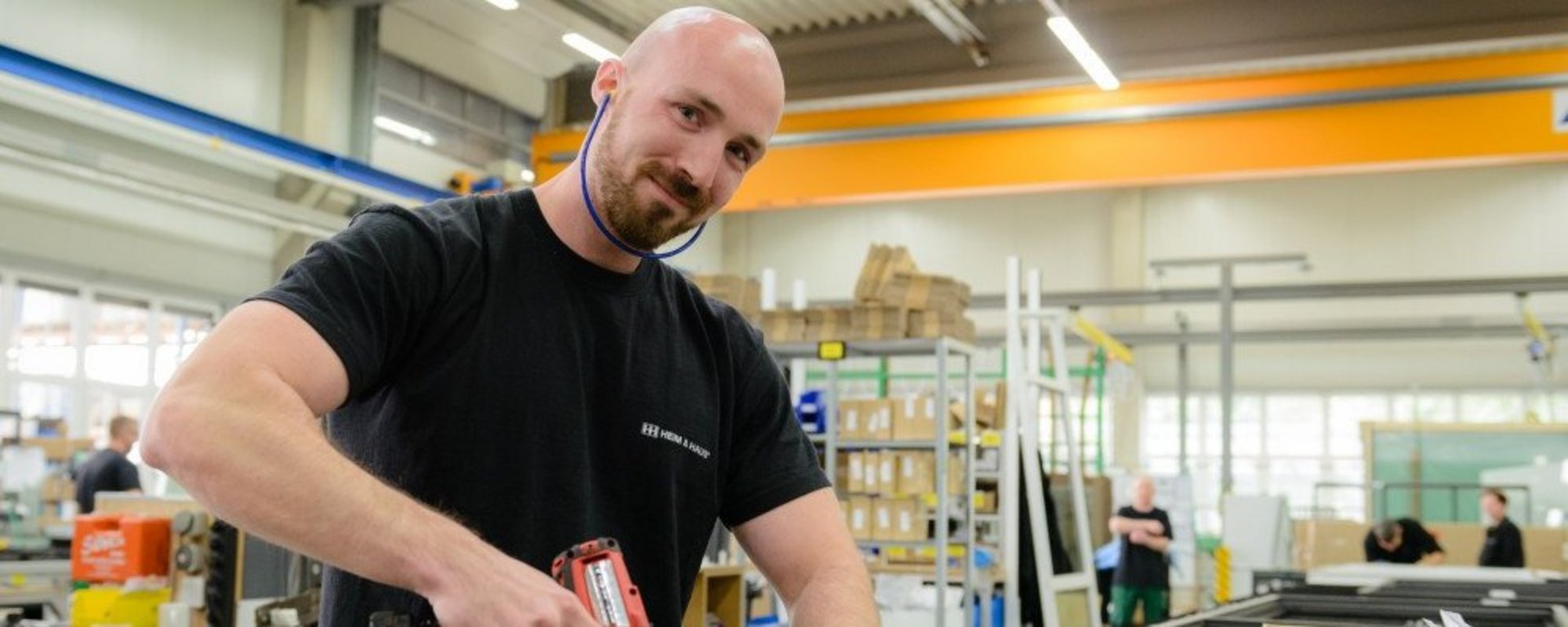 Produktionsmitarbeiter Produktionsstellen HEIM & HAUS Mann mit Akkuschrauber in der Hand, der in die Kamera lacht