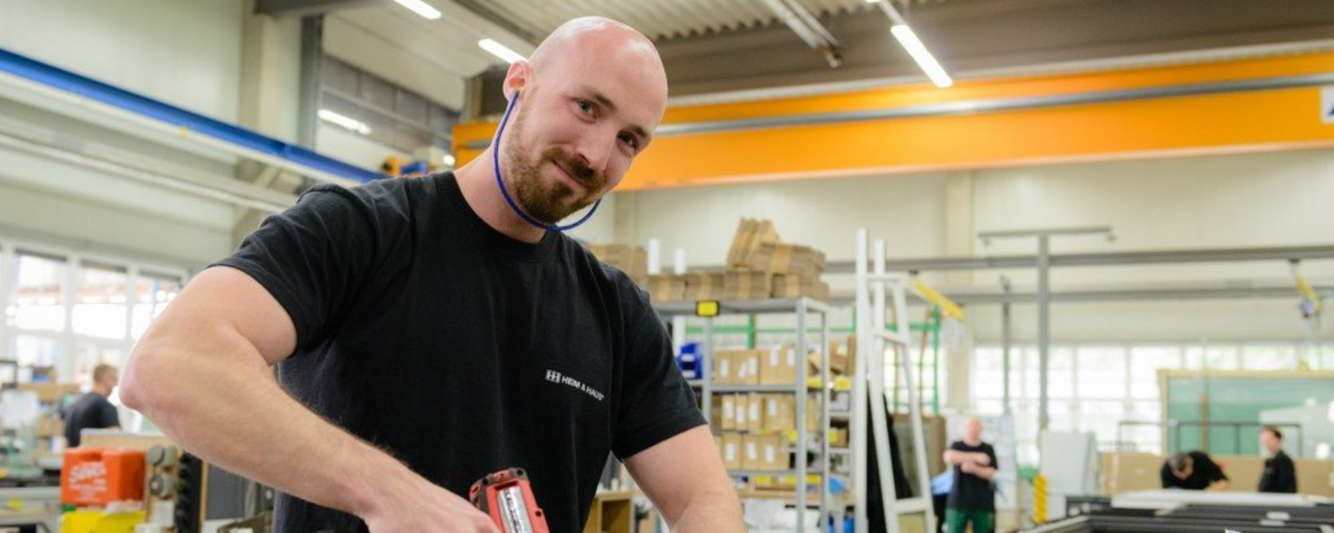 Produktionsmitarbeiter Produktionsstellen HEIM & HAUS Mann mit Akkuschrauber in der Hand, der in die Kamera lacht