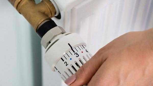 Thermostat bei Abwesenheit oder nachts nicht ganz abdrehen Frauenhand dreht Thermostat an Heizkörper