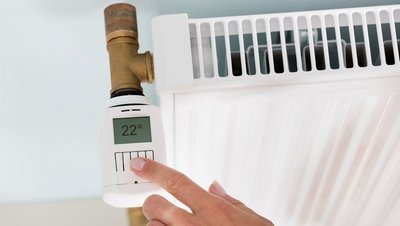 Digitales Thermostat an Heizkörper, Frauenhand stellt Thermostat ein